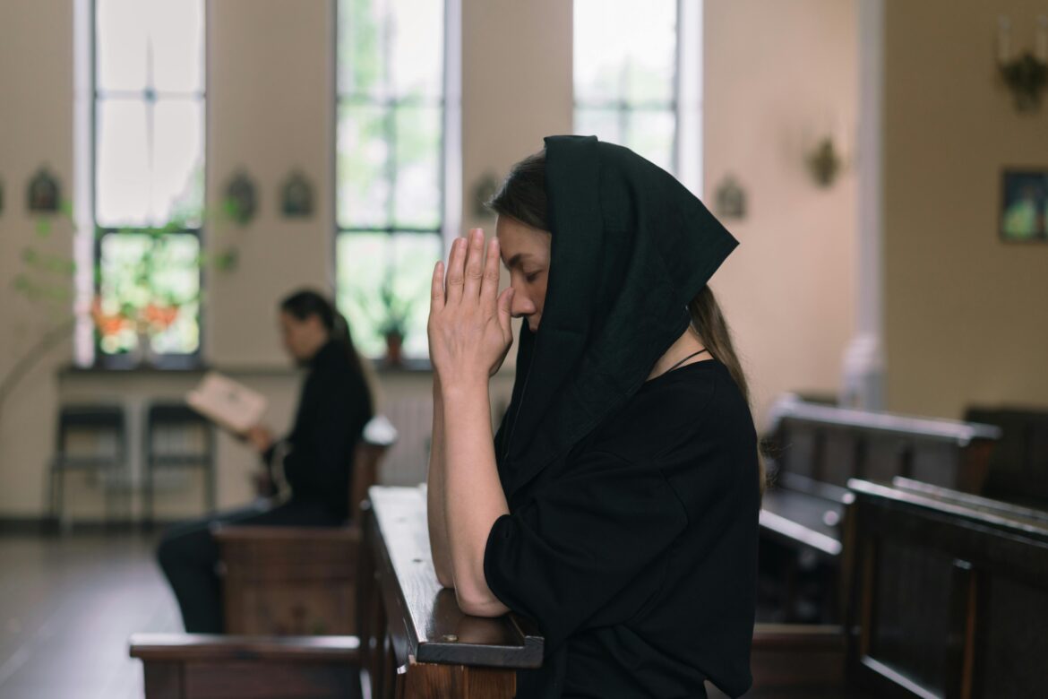 A woman with a veil prays in a serene church setting, reflecting deep spirituality.